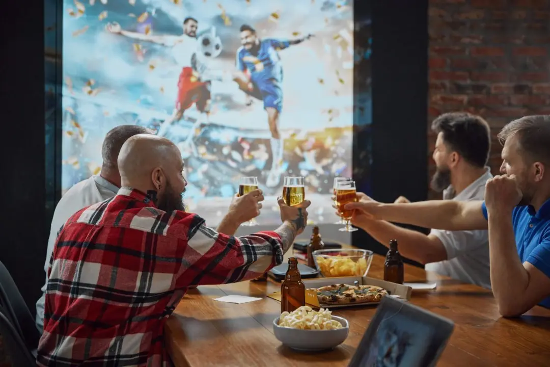 Varias personas siguen un partido de f&uacute;tbol por televisi&oacute;n en un bar | Foto de 123RF/melnyk58